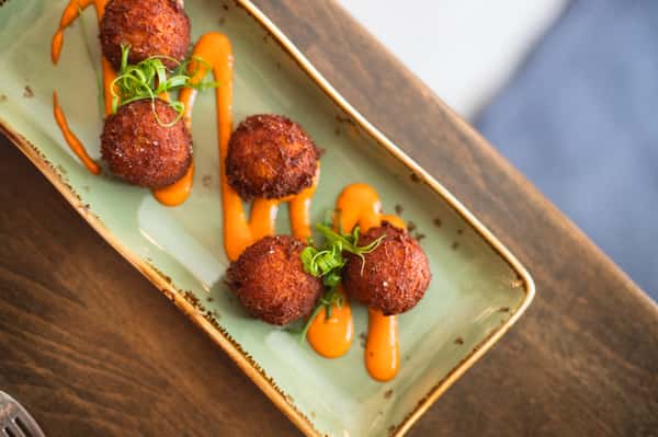 Deep-fried fritters arranged on a green plate with orange sauce swirls and green onion garnish.