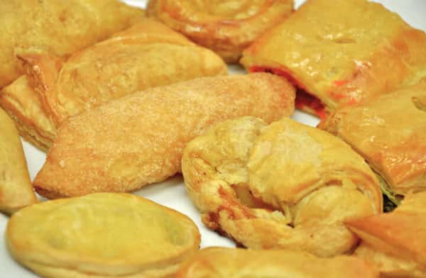 Assorted golden puff pastries and flaky hand pies arranged on a white plate, showcasing buttery layers and a fresh bakery selection of sweet and savory treats.