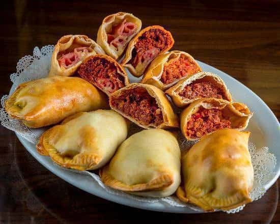Plate of freshly baked empanadas and sliced savory pastry rolls filled with seasoned ground beef and diced vegetables, showcasing golden flaky crusts and authentic Latin bakery presentation.
