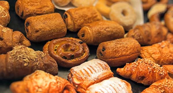 Assorted freshly baked French pastries including golden croissants, pain au chocolat, and raisin swirls displayed on a bakery counter, showcasing flaky layers and a warm, inviting café ambiance.