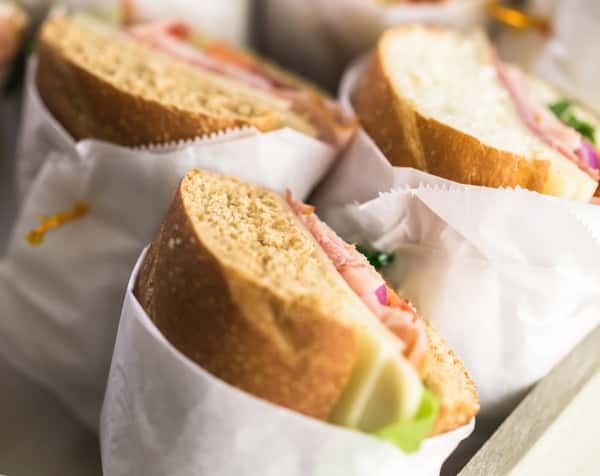 Fresh deli sandwiches on crusty artisan bread with sliced meats, cheese, and crisp lettuce, wrapped in paper for a casual café lunch or gourmet takeaway option.