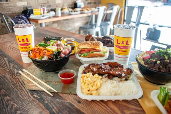 A spread of Hawaiian food on a table including BBQ chicken plate, a poke bowl and a drink