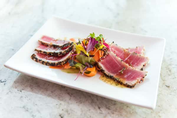 Seared ahi tuna layered with fresh vegetables, vibrant greens, and colorful garnishes for a light, elegant dish packed with fresh coastal flavor.