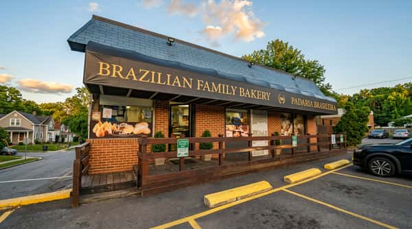 Brazilian Family Bakery storefront with a dark awning, wood railing entrance, and a parked car.