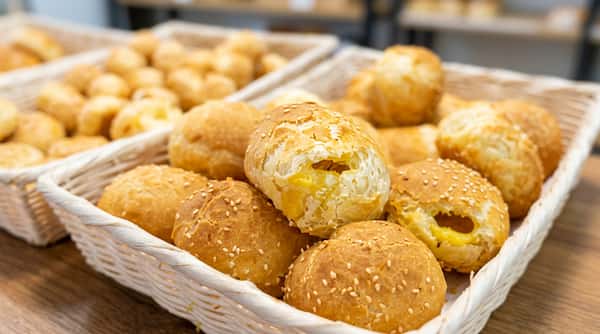 Baked golden pastries, some with sesame seeds, piled in a white woven basket.