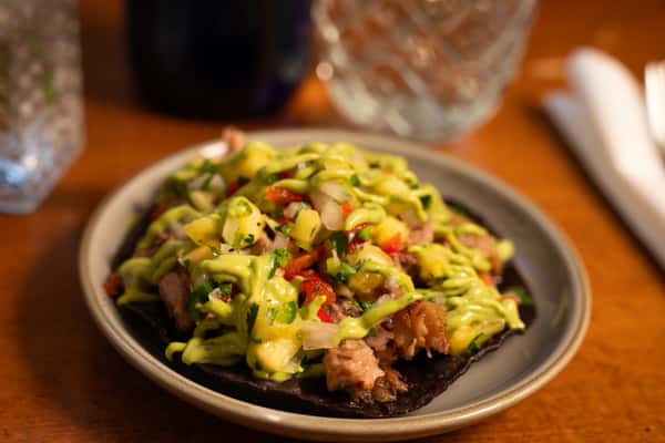 A black corn tortilla topped with grilled meat, fresh salsa, avocado sauce, and cilantro.