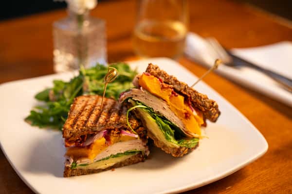 A grilled sandwich with turkey, spinach, roasted squash, red onions, and a slice of cheese, served with a side of arugula salad.
