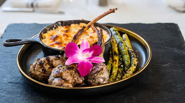 Braised short ribs with grilled asparagus, a side of mac and cheese, and a pink orchid garnish.