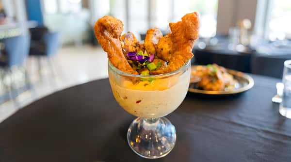 Shrimp and grits served in a glass, topped with fried fish and garnished with green onions and purple edible flowers.