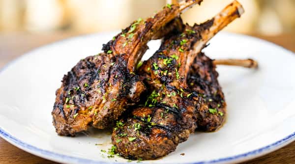 Grilled lamb chops, seasoned and topped with fresh herbs, on a white plate with blue trim.