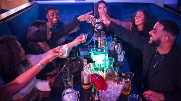 Group of friends celebrating and raising drinks around a table with bottles and glasses.