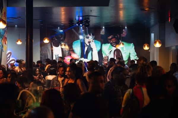 Crowded nightclub with a DJ performing on stage and people dancing.