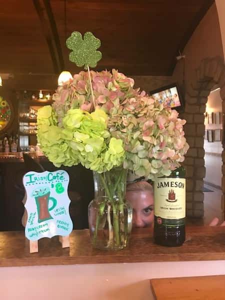 vase of flowers, bottle of jameson, and iced coffee frame on a table