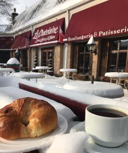 cup of coffee and croissant on a table covered in snow