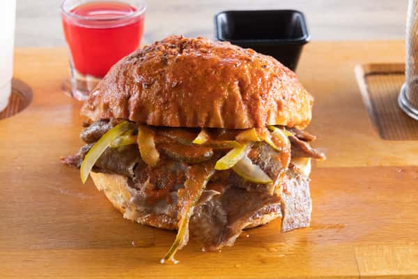 Slow-cooked Mexican pork torta topped with pickled jalapeños, onions, and savory sauce on a toasted artisan bun.