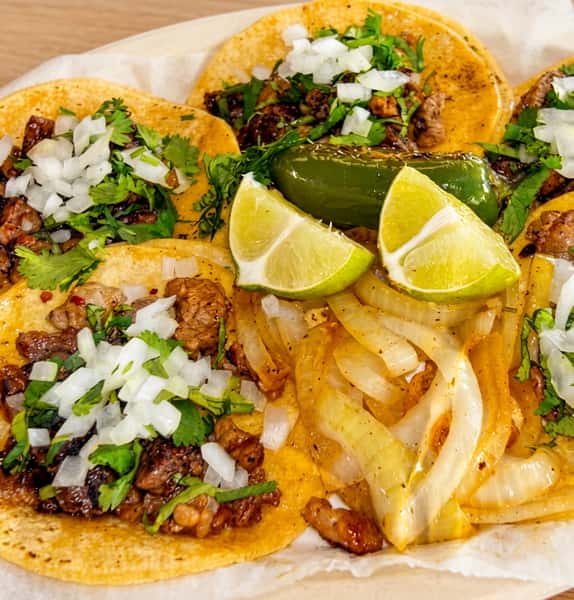 Authentic Mexican street tacos filled with grilled carne asada, topped with fresh cilantro and diced onions, served with grilled jalapeño, sautéed onions, and lime wedges.