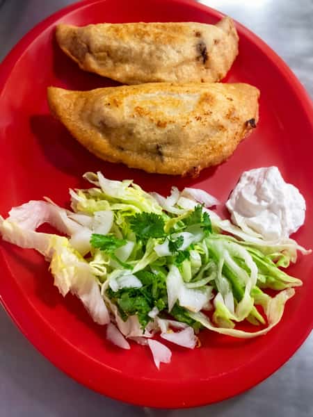 Crispy fried Mexican empanadas served with shredded lettuce, fresh cilantro, and crema on a red plate.