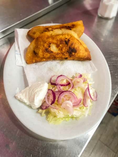 Golden fried empanadas served with shredded lettuce, pickled red onions, and a side of Mexican crema.