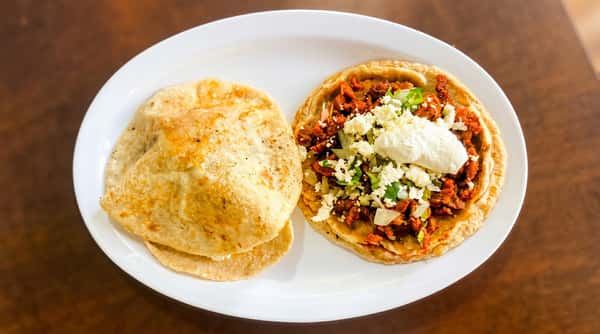 Sope with chorizo, crumbled white cheese, white onions, cilantro, and crema, served with two corn tortillas.
