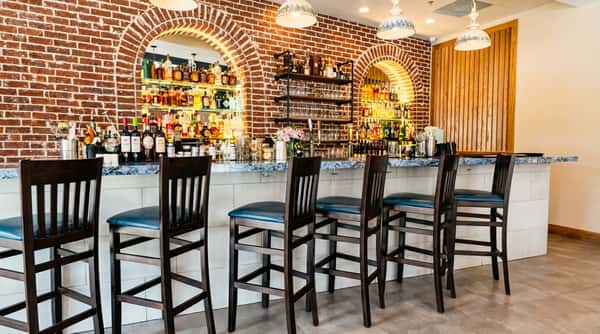 Bar area with exposed brick walls, arched alcoves displaying liquor bottles, and dark wooden bar stools with blue seats.