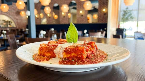 Pasta cannelloni with red sauce, white sauce, Parmesan, and a basil leaf on a white plate.