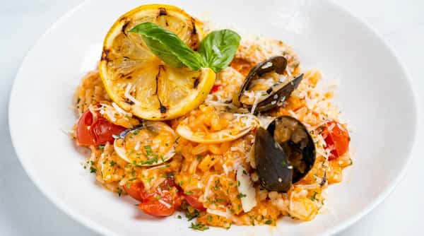 Seafood risotto with clams, mussels, grated cheese, basil, and a charred lemon slice.
