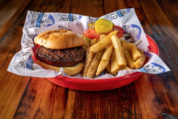 Classic grilled beef burger served with thick-cut seasoned fries, pickles, and fresh tomato slices on a rustic wooden table at a casual American eatery.