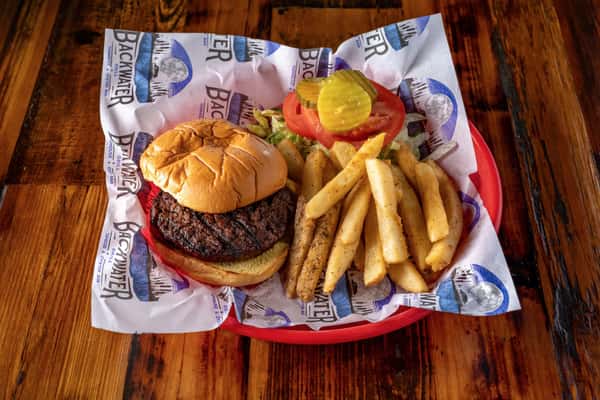 Classic grilled beef burger with fresh tomato, lettuce, and pickles, served with seasoned fries in a laid-back taphouse setting.
