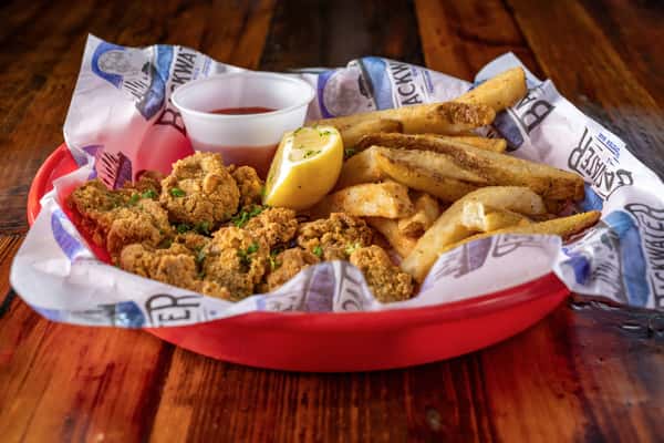 Southern-style fried oysters served with seasoned fries, lemon wedge, and a side of cocktail sauce in a casual seafood restaurant setting.