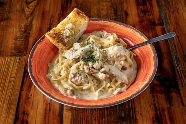 Creamy chicken Alfredo pasta tossed with fettuccine and grilled chicken, topped with herbs and parmesan, served with garlic toast.