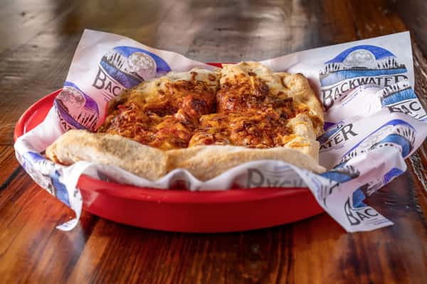 Personal-size flatbread pizza topped with melted cheese and seasoned meats, served in a red basket lined with branded paper.