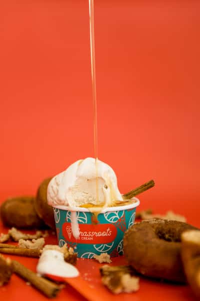 Vanilla ice cream topped with honey drizzle in a cup surrounded by donuts and cinnamon sticks, indulgent dessert scene