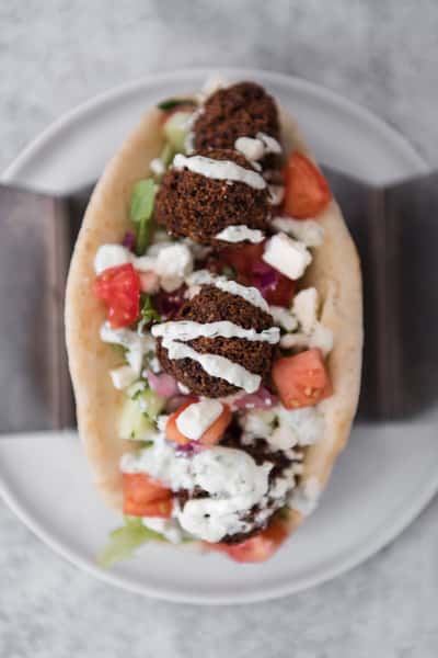 Falafel pita sandwich stuffed with fresh vegetables, feta cheese, and drizzled tzatziki sauce, Mediterranean street food close-up