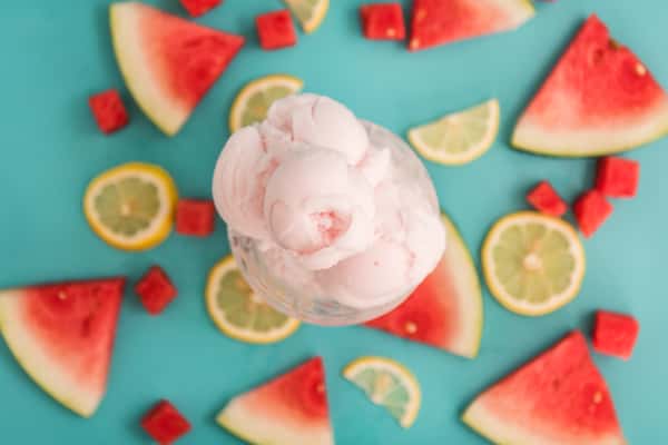 Watermelon and lemon slices surrounding a scoop of pink fruit sorbet on a turquoise background, refreshing summer dessert flat lay