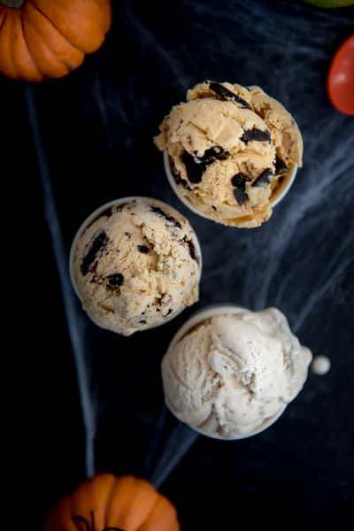Three scoops of cookies and cream and vanilla ice cream on a dark surface with small pumpkins, seasonal autumn dessert presentation