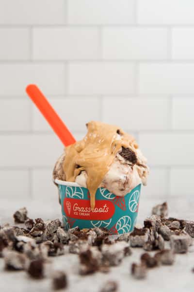 Cookies and cream ice cream scoop in a branded cup topped with peanut butter drizzle and cookie crumbles, dessert shop presentation