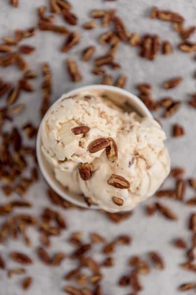 Vanilla ice cream with pecans in a cup surrounded by scattered nuts, rich nutty dessert overhead shot
