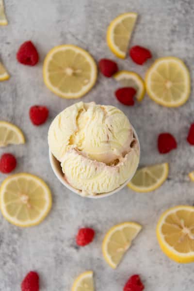 Lemon ice cream scoop in a cup with fresh raspberries and lemon slices, bright citrus dessert overhead