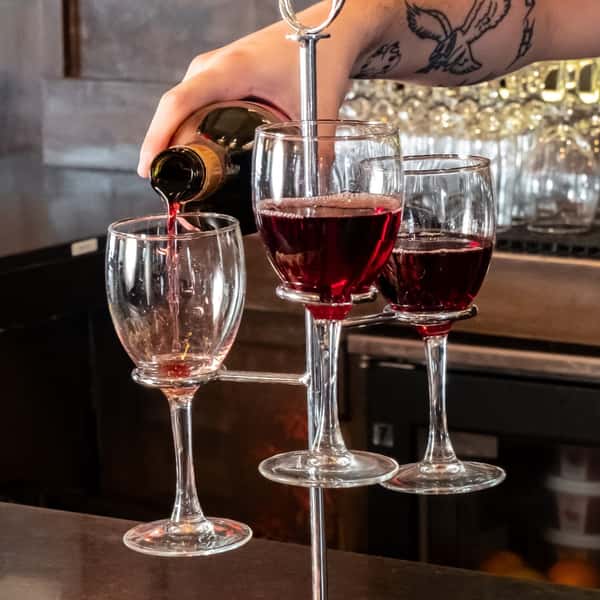 Close-up of a bartender pouring red wine into a creative vertical wine flight display featuring four wine glasses—elegant presentation perfect for wine tastings or upscale happy hour.