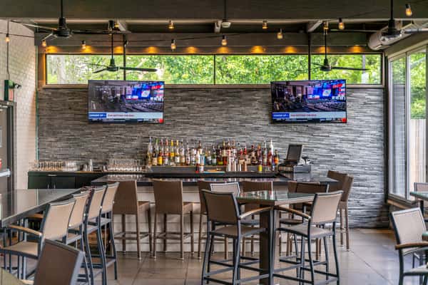 ontemporary bar setup with stone backsplash, high-top seating, dual flat-screen TVs, and an array of premium liquors; ideal sports bar setting with a sleek, modern vibe.