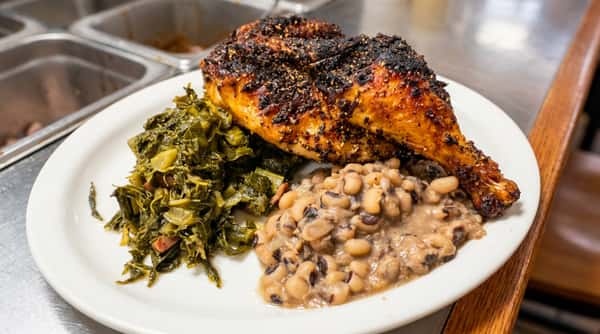 Baked chicken leg and thigh with crispy seasoned skin, served with collard greens and black-eyed peas.