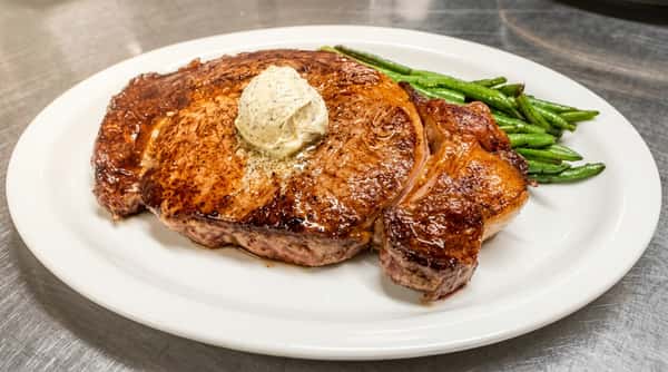 Cooked steak with a dollop of herb butter and a side of green beans on a white plate.
