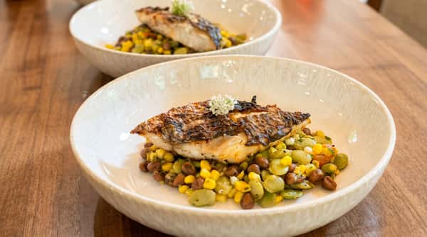 Two bowls of fish with seared skin, served over a colorful succotash of corn, lima beans, and black beans.