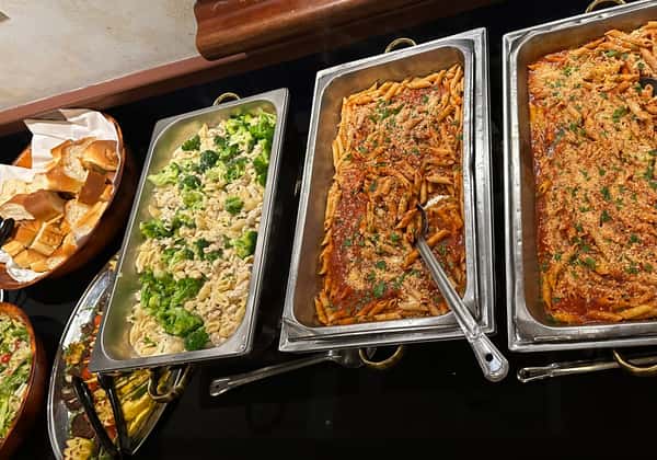 Italian buffet with garlic bread, creamy chicken and broccoli pasta, baked penne with marinara, and mixed green salad.