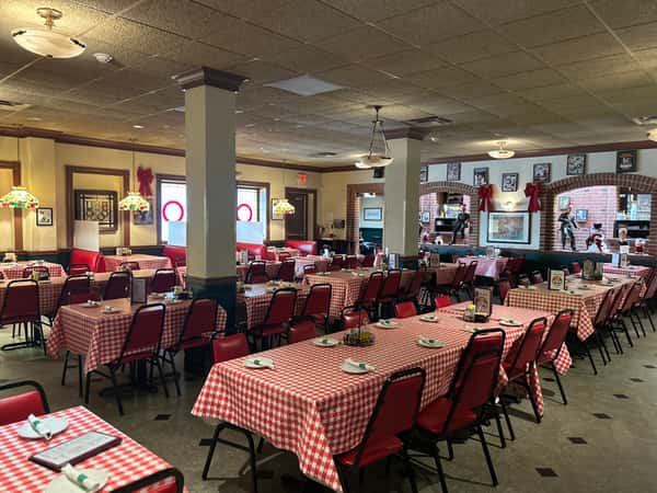 Classic Italian dining room with red-checkered tablecloths, vintage pendant lighting, and family-style seating arrangement.