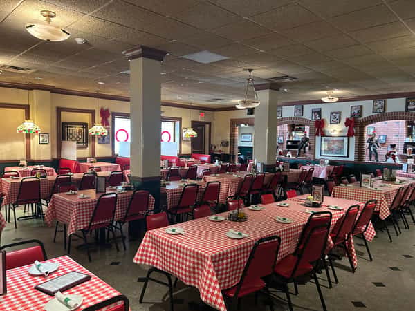 Spacious Italian-American restaurant dining room with red-checkered tablecloths, red chairs, and classic decor for a cozy ambiance.