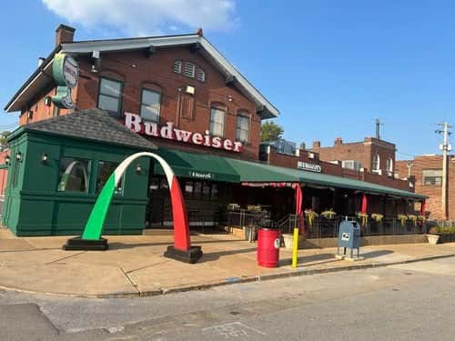 Exterior of Rigazzi's restaurant with a red-brick facade, Budweiser signage, and a green, white, and red Italian-themed arch.