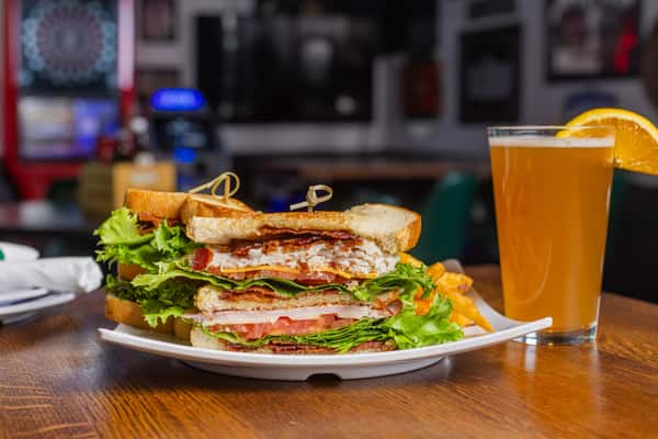 Triple-decker club sandwich layered with turkey, bacon, lettuce, and tomato, served with a cold draft beer.
