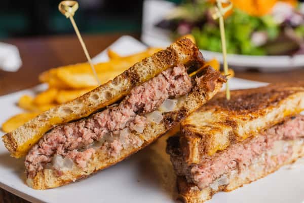 Close-up of a juicy patty melt sandwich with seasoned beef and melted cheese on grilled rye bread.
