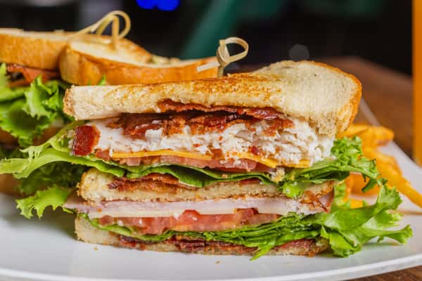 Close-up of a stacked club sandwich with sliced turkey, crispy bacon, fresh lettuce, and tomato.